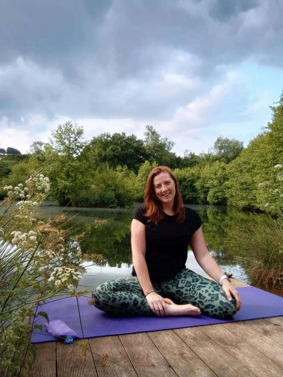 Liv seated on her purple yoga mat beside the water